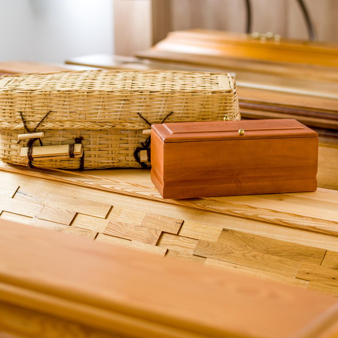 Holzkisten, eine aus Weide und eine aus Holz, liegen auf mehreren hölzernen Särgen in einem Raum.