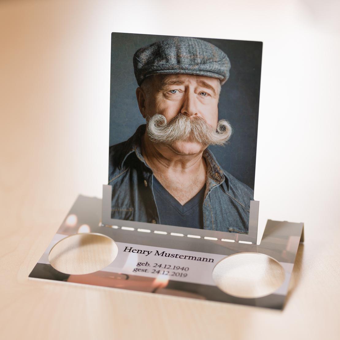 Portrait eines Mannes mit Schnurrbart und Mütze in einem Bilderhalter, mit Inschrift über Geburts- und Sterbedaten.