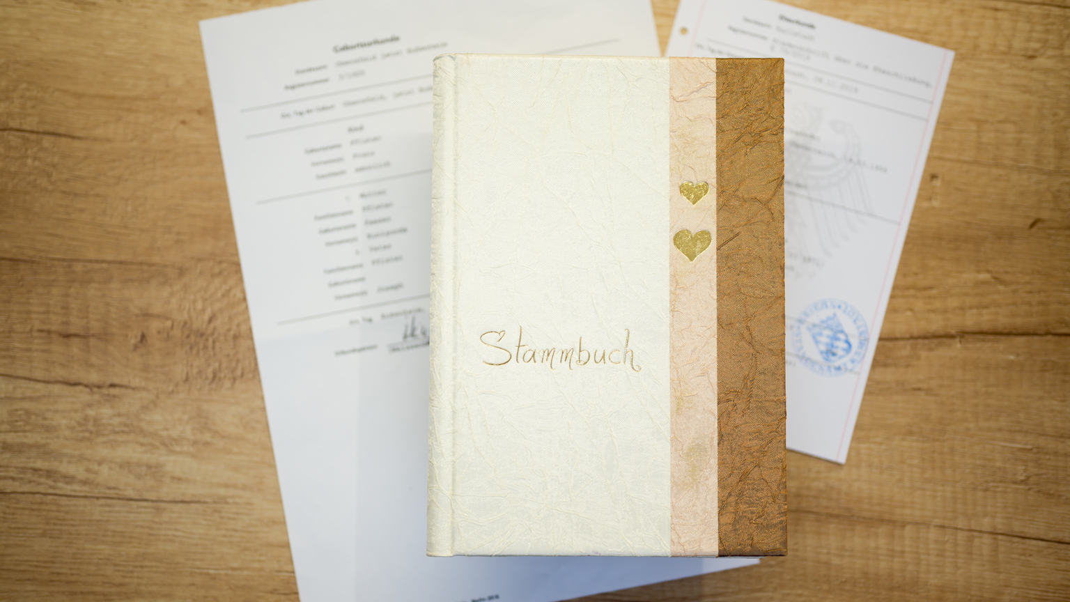 Stammbaum-Buch auf einem Holztisch, umgeben von offiziellen Dokumenten zur Geburt.