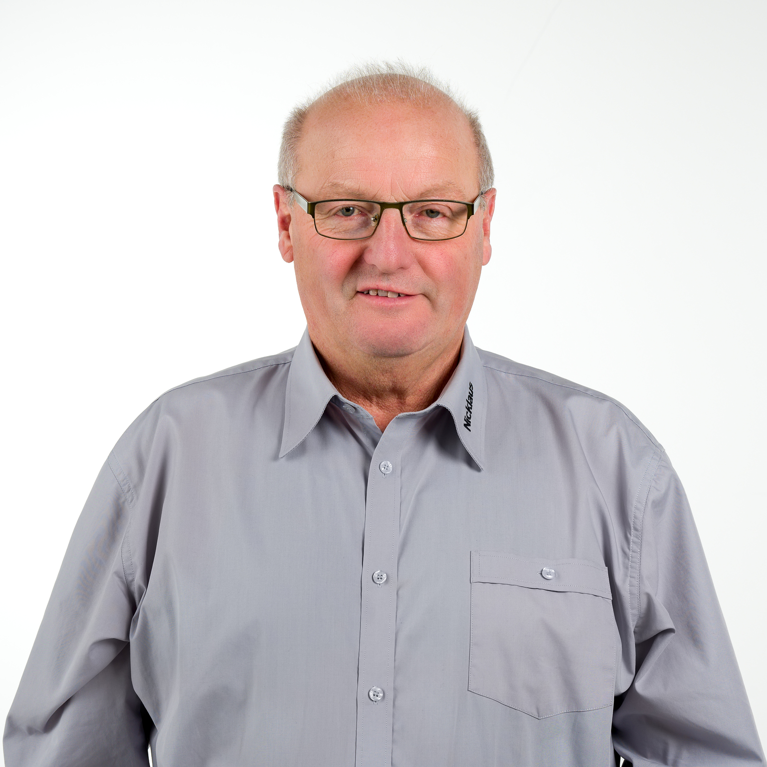 Porträt eines Mannes mit Brille, grauhem Hemd und kurzen Haaren, vor einem weißen Hintergrund.