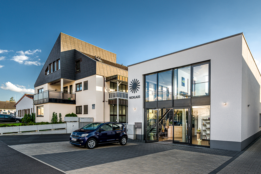 Moderne Gebäude mit Glasfassade und Treppe, davor ein blauer Smart und eine gepflegte Landschaft im Hintergrund.