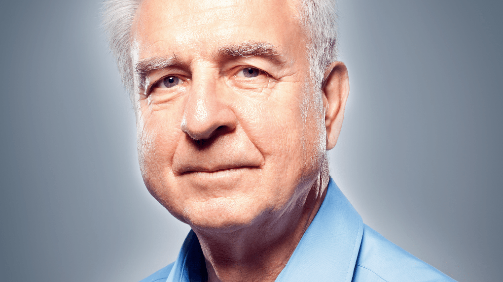 Porträt eines älteren Mannes mit grauem Haar, der in einem hellblauen Hemd freundlich in die Kamera schaut.