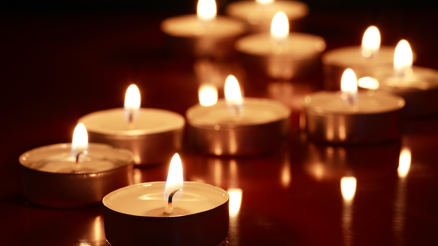 Eine Reihe brennender Teelichter auf einer reflektierenden Oberfläche in dunkler Umgebung.