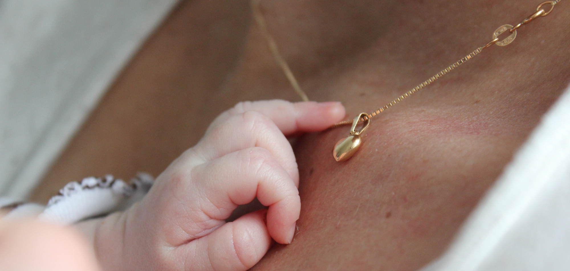 Babyhand greift sanft nach einer goldenen Halskette mit Anhänger auf der Haut einer Person.